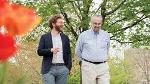 Professors Nuno Moniz and Don Howard walk on campus in the spring, talking together.